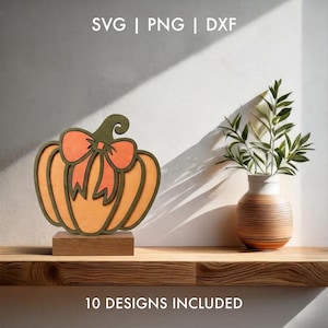 Puede incluir: Un recorte de calabaza de madera en capas con un cuerpo de color naranja claro, un contorno verde oliva oscuro y un lazo naranja a juego en la parte superior, montado sobre una base rectangular. El texto SVG | PNG | DXF y 10 DESIGNS INCLUDED aparece.