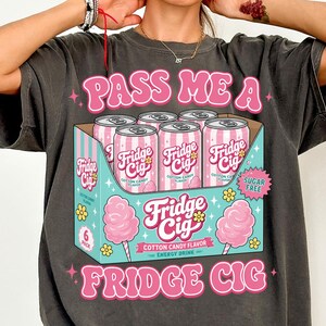 Op de afbeelding: Een antracietgrijs t-shirt met een afbeelding van een sixpack roze-wit gestreepte blikjes met het label Fridge Cig Cotton Candy flavor. Het ontwerp bevat roze tekst Pass Me A Fridge Cig, kleine gele bloemen, roze suikerspinillustraties en een sterretje met de tekst Sugar Free.
