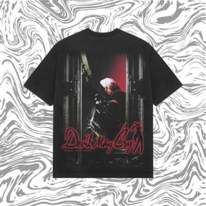 May include: Black t-shirt featuring a graphic from the video game "Devil May Cry." The design includes a character with white hair, a gun, and the game's logo in red. The Japanese text is also visible.