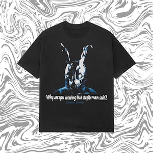 May include: Black t-shirt with a blue and white graphic of a rabbit-like figure and the text "Why are you wearing that stupid man suit?" and "Donnie Darko". The shirt has a crew neck and short sleeves.
