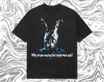 May include: Black t-shirt featuring a blue and white graphic of a rabbit-like figure with the text "Why are you wearing that stupid man suit?" and "Donnie Darko". The shirt has a crew neck and short sleeves.