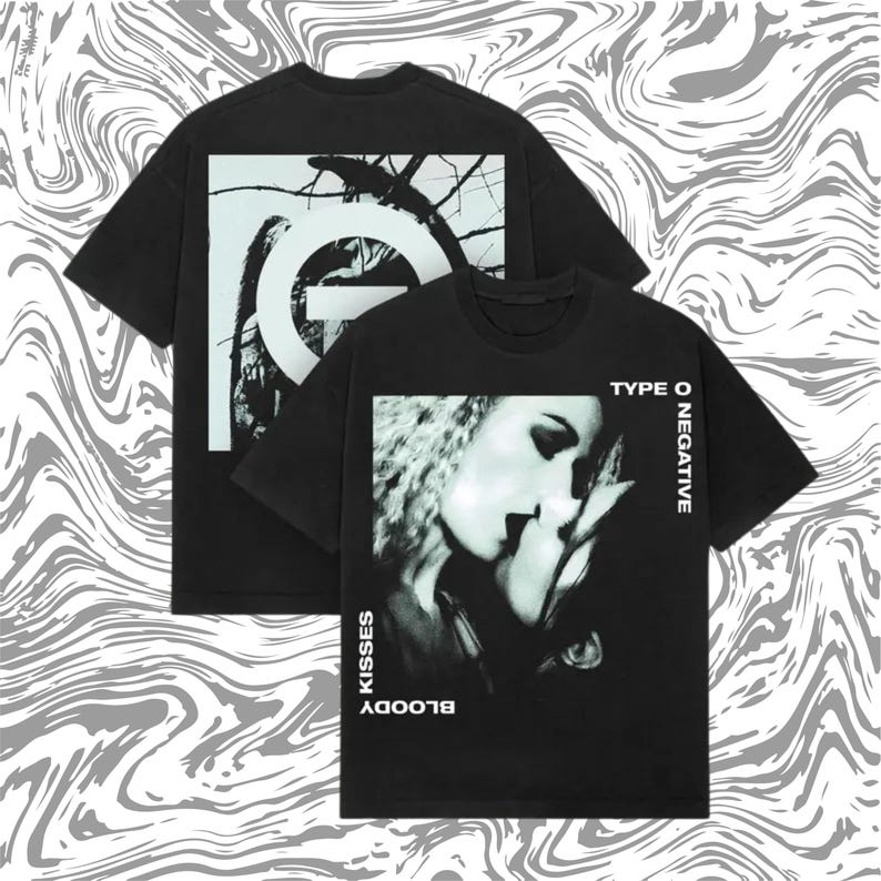 May include: Two black t-shirts with white graphics. One features a tree branch design with a large letter "O". The other displays a black and white image of a couple kissing, with the words "TYPE O NEGATIVE" and "BLOODY KISSES".