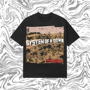 Puede incluir: Una camiseta negra de manga corta con un estampado gráfico rectangular de una ladera, el texto "SYSTEM OF A DOWN" en letras blancas y la palabra "TOXICITY" en letras rojas en la parte inferior derecha del diseño gráfico.
