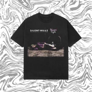May include: Black t-shirt with the text "SILENT HILL 2 Enhanced Edition" and "Heaven's Night". The graphic shows a person in purple attire lying down. The tee has a crew neck and short sleeves.