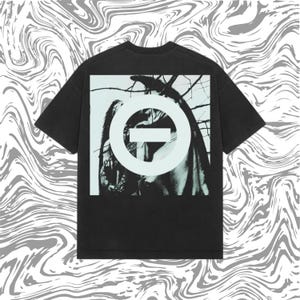 May include: Black t-shirt featuring a graphic design on the back. The design includes a white circle with a horizontal line through it, set against a black and white image. The shirt has short sleeves and a crew neck.