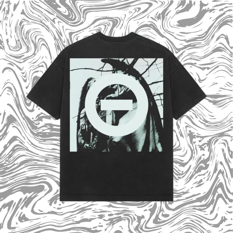 May include: Black t-shirt featuring a graphic design on the back. The design includes a white circle with a horizontal line through it, set against a black and white image. The shirt has short sleeves and a crew neck.