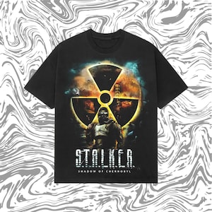 Könnte beinhalten: Schwarzes T-Shirt mit einer Grafik einer Person in einem Schutzanzug, einem gelben Strahlungssymbol und dem Text "STALKER: Shadow of Chernobyl". Das Design hat ein postapokalyptisches Thema.