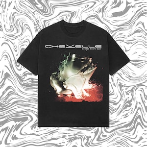 May include: Black t-shirt featuring the band name "Chevelle" above a graphic of a shattered glass. The text "Wonder What's Next" is below the band name. The design has red and green accents.