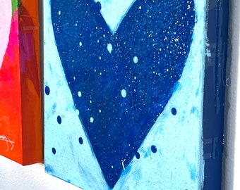 May include: A blue heart with white dots on a light blue background. The heart is painted with glitter and has a blue border. The painting is signed "Jenny" in the bottom right corner.