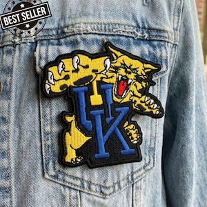 May include: Light blue denim jacket with a patch featuring a yellow wildcat with blue and black lettering. The patch is on the pocket of the jacket. A "BEST SELLER" sticker is on the jacket.