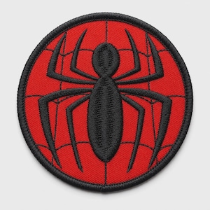 May include: A circular embroidered patch featuring a vibrant red background with a black spider emblem centered in the middle. The design includes a black stitched spiderweb pattern radiating across the red surface, finished with a black border.