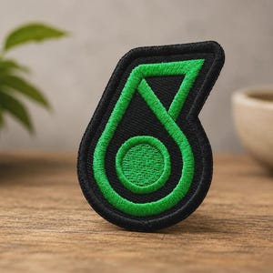 May include: An embroidered patch featuring a stylised number six in vibrant green thread against a solid black background. The design has a thick black border and a circular centre, with clean, dense stitching throughout the entire shape.