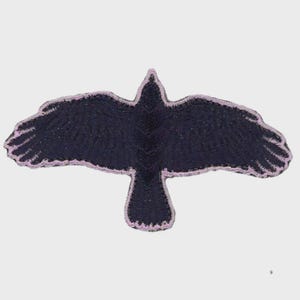 May include: Embroidered patch in the shape of a crow with outstretched wings. The crow is black with a light purple outline. The patch is likely for clothing or accessories.