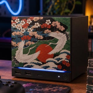 May include: A black desktop computer case featuring a front panel with a detailed graphic print of two white cranes, a large red sun, and blooming cherry blossom trees. The base includes two USB ports, a power button, and a blue LED light strip.