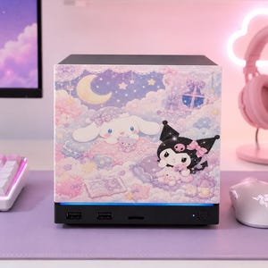 Może przedstawiać: Czarna obudowa komputera z ozdobnym panelem przednim przedstawiającym pastelową ilustrację postaci Cinnamoroll i Kuromi wśród chmur, gwiazd i półksiężyca. Podstawa zawiera dwa porty USB oraz przycisk zasilania z niebieskim podświetleniem.