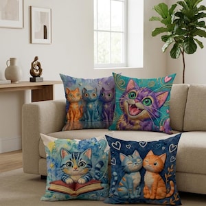 May include: Five decorative cushions with cat illustrations. The cushions feature colourful images of cats in different poses, such as reading, smiling, and cuddling. The colour scheme includes blues, oranges, purples, and greens.