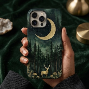 May include: A dark green phone case featuring a forest scene with a golden crescent moon, deer, and mushrooms. The case has a matte finish and is held in a hand. The design includes tall pine trees and a starry night sky.