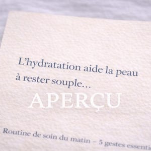 May include: A light beige card with French text. The text reads "L'hydratation aide la peau à rester souple... APERÇU" in dark blue. Below, smaller text reads "Routine de soin du matin - 5 gestes essentiels."