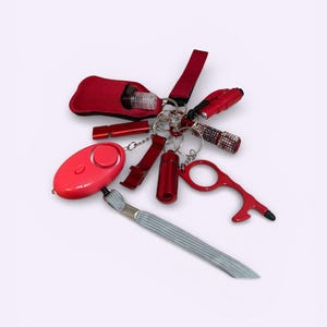 May include: A collection of red safety and convenience items on keychains. Includes a personal alarm, a small torch, a bottle holder, a whistle, a bottle opener, and a no-touch tool. A grey lanyard is also included.
