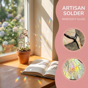 Puede incluir: Una maceta de terracota con una planta suculenta y una decoraci&oacute;n de gato y hongo de vidriera se encuentra en un alf&eacute;izar de madera. El texto "ARTISAN SOLDER IRIDESCENT GLASS" es visible. Un libro abierto est&aacute; en el alf&eacute;izar.