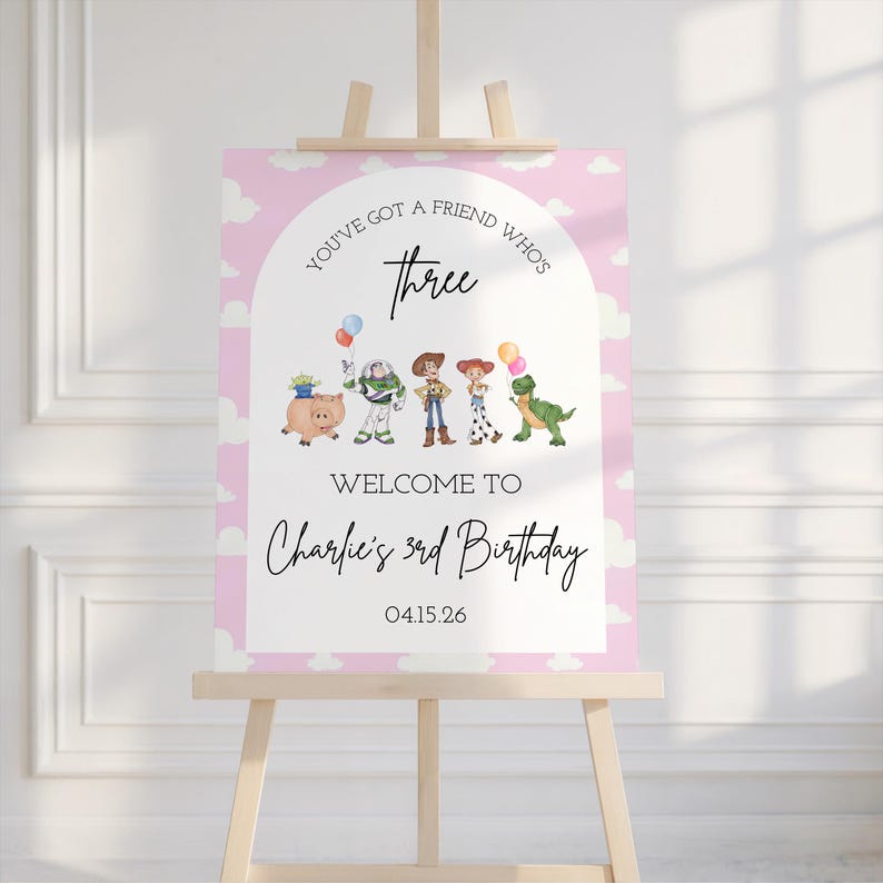 May include: A pink and white welcome sign on a wooden easel. The sign features the text "You've got a friend who's three" and "Welcome to Charlie's 3rd Birthday" with cartoon character illustrations. The date 04.15.26 is also included.