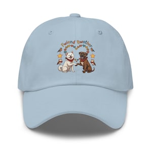 May include: Light blue baseball cap featuring an illustration of two dogs shaking paws, surrounded by hearts, stars, and owls. The text "Fwiend Bwother" is arched above the dogs. The cap has a curved brim and a button on top.