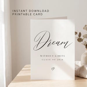 Può includere: Una scheda stampabile bianca con la parola "Dream" in elegante scrittura. Sotto, si legge "Without Limits, Class of 2026" con un piccolo cuore. La scheda è su un tavolo di legno, accanto a un vaso con fiori secchi.