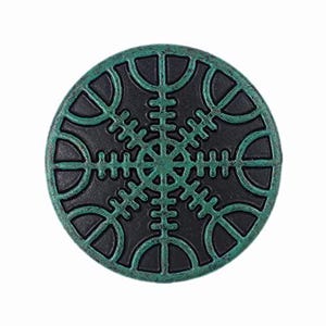 May include: A circular button featuring a black base with a raised, textured green Vegvisir symbol. The design consists of a central point with eight radiating arms, each ending in a curved line, creating a compass-like pattern on the surface.