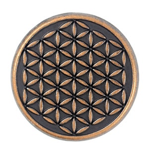 Op de afbeelding: Een ronde, koperkleurige metalen schijf met een zwart, reliëf geometrisch ontwerp van een levensbloem.