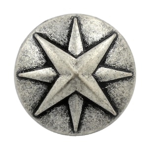 May include: A circular metal button featuring a raised eight-pointed star design. The surface has a distressed, antique silver finish with dark, recessed areas between the star points and along the textured edges of the round button face.