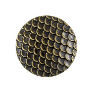 Op de afbeelding: Een ronde knop met een verhoogd, herhalend schubbenpatroon over het oppervlak. Het ontwerp is afgewerkt in een donkere, geoxideerde bronstint met lichtere, goudkleurige metallic accenten op de randen van elke individuele schub.