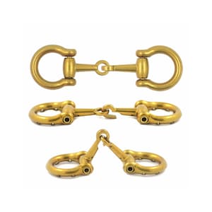 Puede incluir: Un conjunto de tres conectores de bocado para caballo de metal en tono latón, mostrados desde diferentes ángulos. Cada pieza presenta dos bucles circulares conectados por un mecanismo de bisagra central, con acabado mate y remaches.