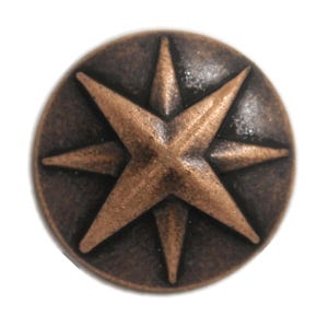 May include: A circular metal button featuring a raised eight-pointed star design in a dark bronze finish. The surface has a weathered, textured appearance with lighter highlights on the star points and a darker, recessed background.