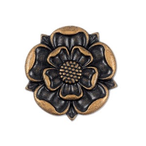 Puede incluir: Un emblema metálico circular con forma de flor de cinco pétalos. El diseño presenta un centro oscuro hundido y bordes texturizados en relieve con un acabado en tono bronce metálico. La parte central muestra un patrón de puntos.