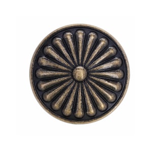 Op de afbeelding: Een ronde metalen knoop met een verhoogd, zonachtig patroon en een centraal cirkelvormig element. Het ontwerp bestaat uit uitstralende bloemblaadjes in een gebruinde bronsafwerking tegen een verzonken, zwarte achtergrond.