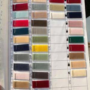 May include: A fabric swatch color chart featuring a grid of numbered rows and columns. Each cell contains a small rectangular piece of mesh fabric in various colors, including red, blue, green, yellow, beige, and gray, attached with a metal staple.