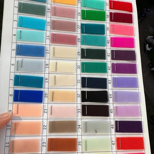 May include: A color swatch chart featuring forty-eight rectangular samples of fine mesh fabric arranged in a grid. Each fabric swatch is numbered and secured with a metal staple to a white paper sheet containing columns for product name, weight, and width.
