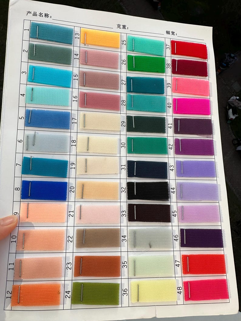 May include: A color swatch chart featuring forty-eight rectangular samples of fine mesh fabric arranged in a grid. Each fabric swatch is numbered and secured with a metal staple to a white paper sheet containing columns for product name, weight, and width.