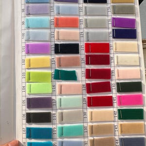 May include: A fabric swatch color chart featuring a grid of numbered tulle samples in various colors including blue, purple, pink, red, green, yellow, and neutral tones. Each rectangular mesh fabric piece is attached to a white paper sheet.