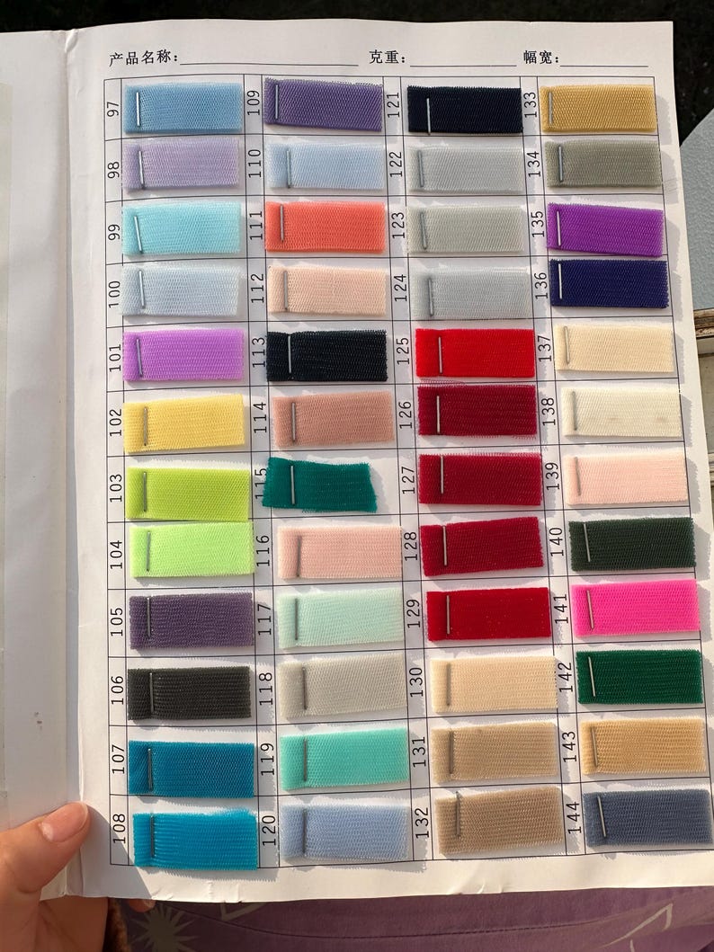 May include: A fabric swatch color chart featuring a grid of numbered tulle samples in various colors including blue, purple, pink, red, green, yellow, and neutral tones. Each rectangular mesh fabric piece is attached to a white paper sheet.