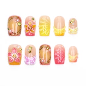 May include: A set of ten press-on nails featuring a variety of designs in shades of pink, yellow, and orange. The nails are decorated with three-dimensional floral accents, gold wire swirls, small white pearls, and metallic gold beads.