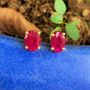 Peut inclure: Une paire de boucles d'oreilles à clous avec des rubis rouges de taille ovale montés sur des griffes en or jaune. Chaque pierre précieuse présente une surface à facettes qui reflète la lumière, révélant une teinte cramoisie profonde.