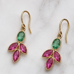 May include: A pair of gold-tone drop earrings featuring a single oval-shaped green gemstone at the top, connected to three smaller marquise-shaped pink gemstones arranged in a leaf-like pattern, suspended from curved gold-tone ear wires.