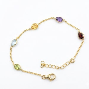 Peut inclure: Un bracelet en or orné de sept pierres précieuses en forme de goutte, de couleurs jaune, bleu, vert, violet et rouge. Le bracelet est doté d'une chaîne délicate et d'un fermoir mousqueton. Les pierres sont espacées uniformément.