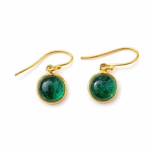 Puede incluir: Un par de pendientes dorados con una piedra redonda de color verde esmeralda. Los pendientes tienen un diseño de gancho simple y un acabado pulido. Las piedras verdes están engastadas en un bisel dorado.