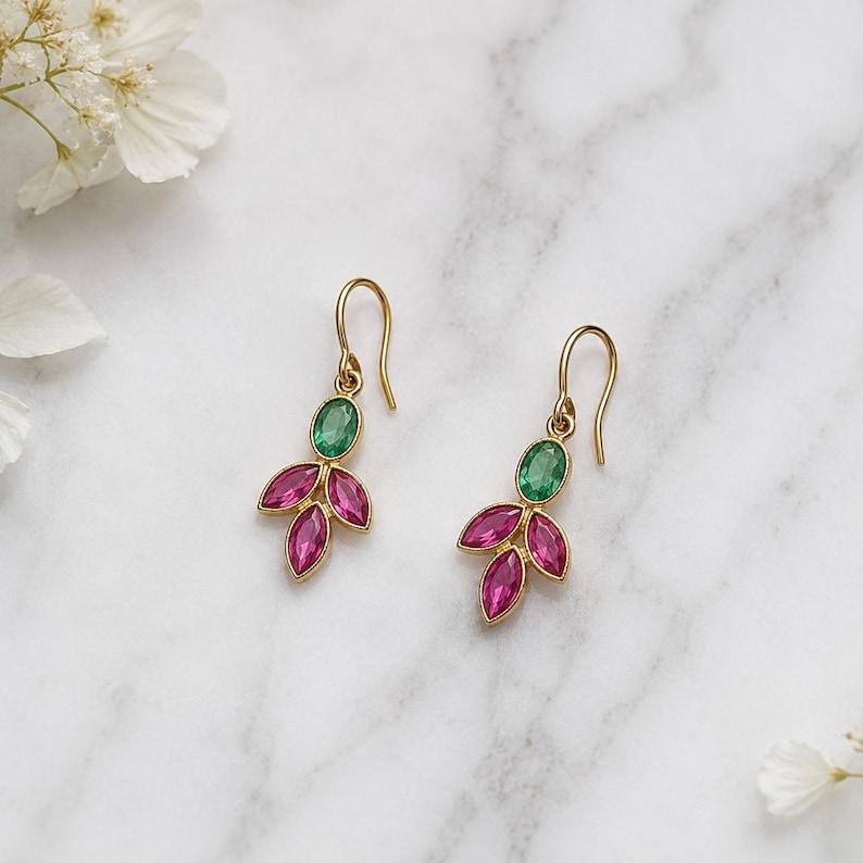May include: A pair of gold-tone drop earrings featuring a single oval-shaped green gemstone at the top, connected to three smaller marquise-shaped pink gemstones arranged in a leaf-like pattern, suspended from curved gold-tone ear wires.