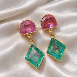 Può includere: Un paio di orecchini pendenti con montatura dorata. Ogni orecchino presenta una pietra rosa a semicerchio nella parte superiore, collegata tramite un piccolo anello d'oro a una pietra verde a forma di rombo nella parte inferiore.