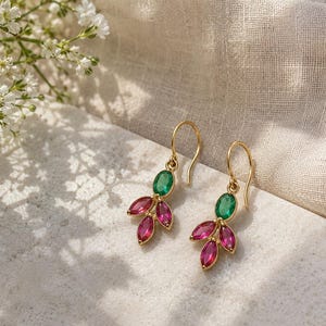 May include: A pair of gold drop earrings featuring a single oval-cut green gemstone at the top, accented by three marquise-cut pink gemstones arranged in a leaf-like cluster at the bottom, suspended from simple gold ear wires.