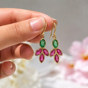 May include: A pair of gold-tone drop earrings featuring a single oval green gemstone at the top and three marquise-shaped pink gemstones arranged in a fan pattern below, suspended from a curved gold-tone hook wire for pierced ears.