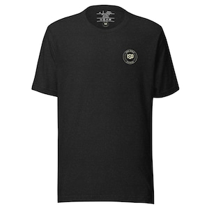 Puede incluir: Camiseta negra con cuello redondo. Presenta un pequeño logotipo circular en el pecho izquierdo con el texto "ISD Division" en dorado. La camiseta está hecha de una tela suave y texturizada. Una prenda clásica y cotidiana.